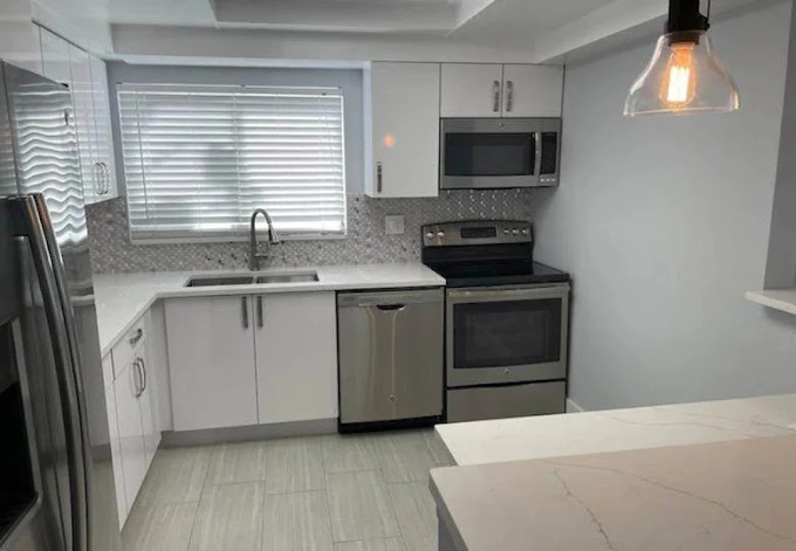Modern kitchen with white cabinets, stainless steel appliances, and a window with blinds.