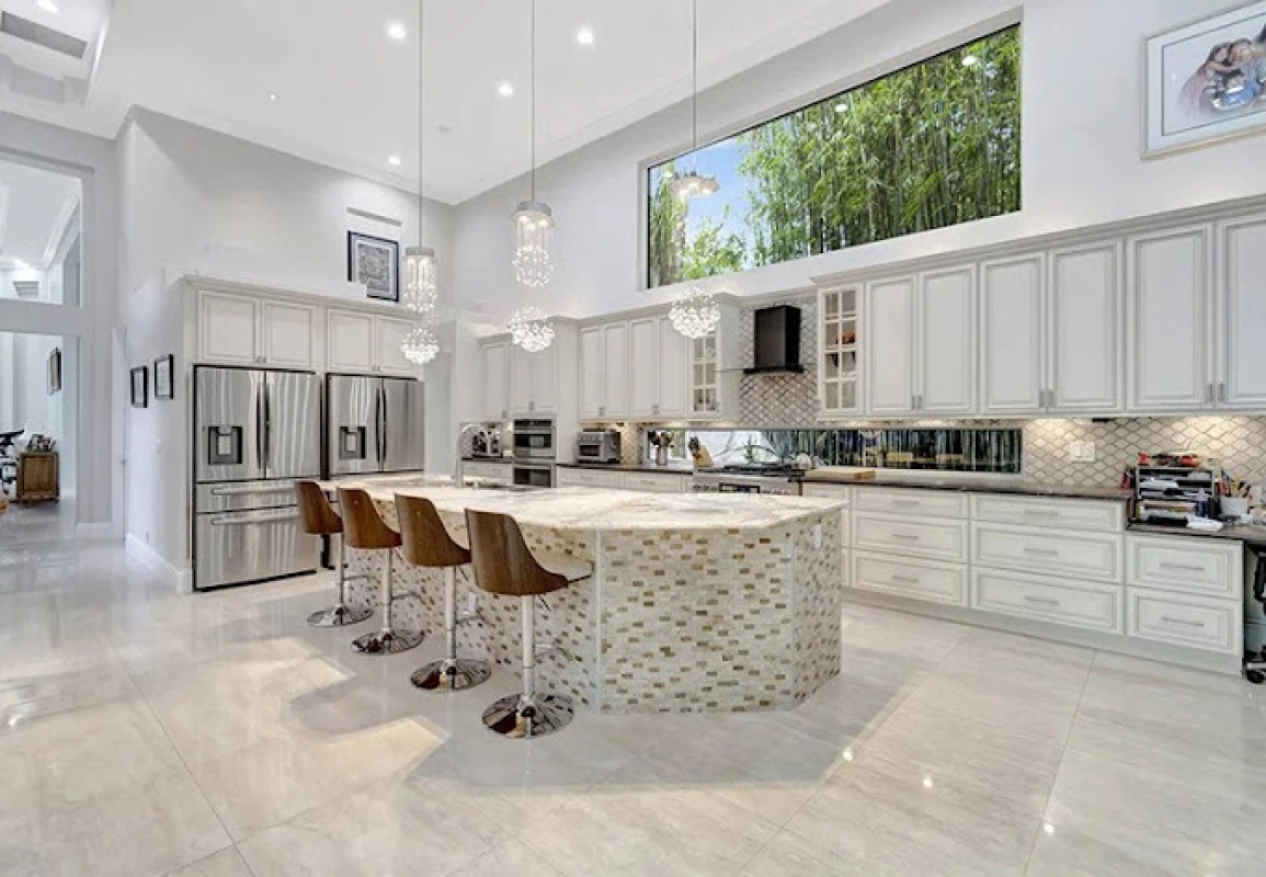 Spacious white kitchen with a large island and high ceilings, featuring a large window with a bamboo view.