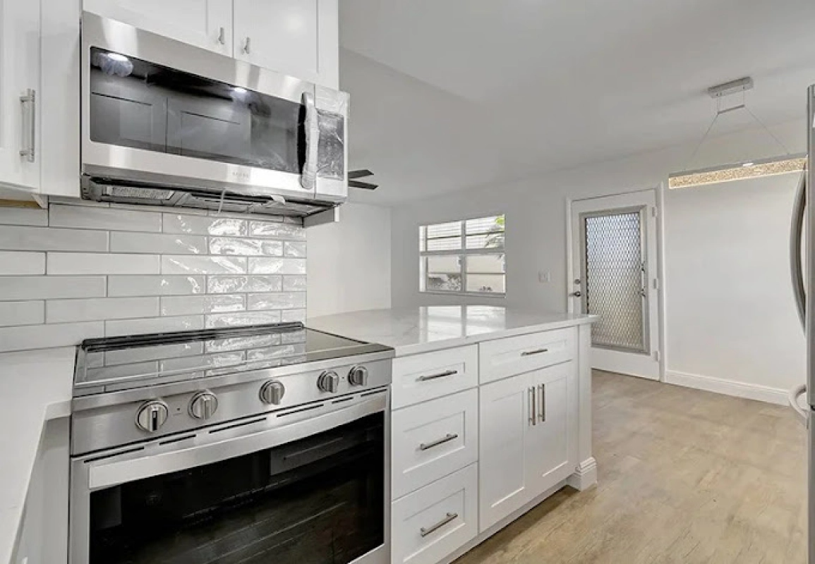 Modern white kitchen with stainless steel appliances, island, and door to outside.