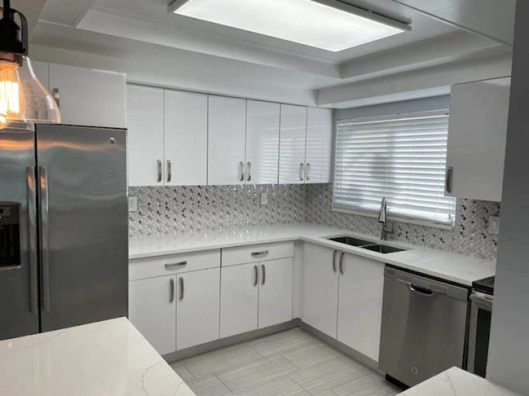 White kitchen with stainless steel appliances, white cabinets, and a patterned backsplash.