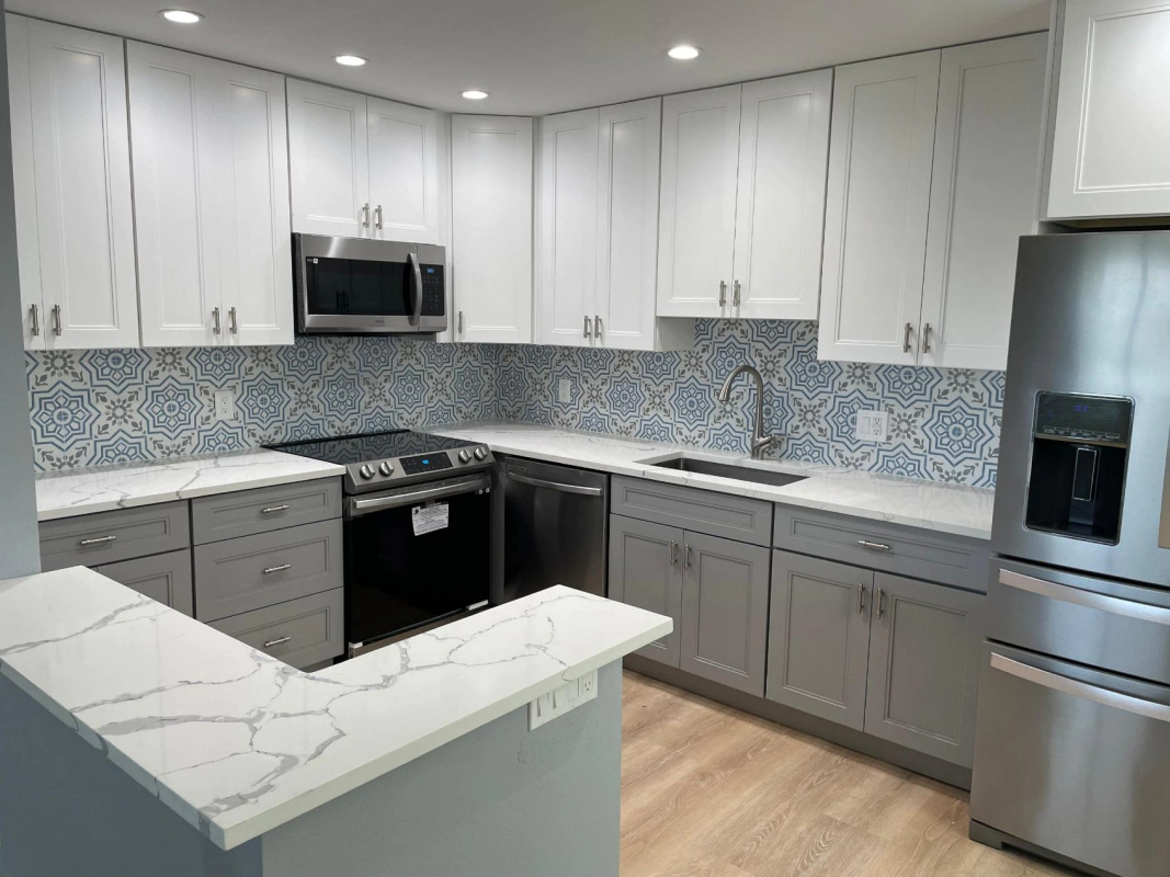 Modern kitchen with white and gray cabinets, blue patterned backsplash, and stainless steel appliances.