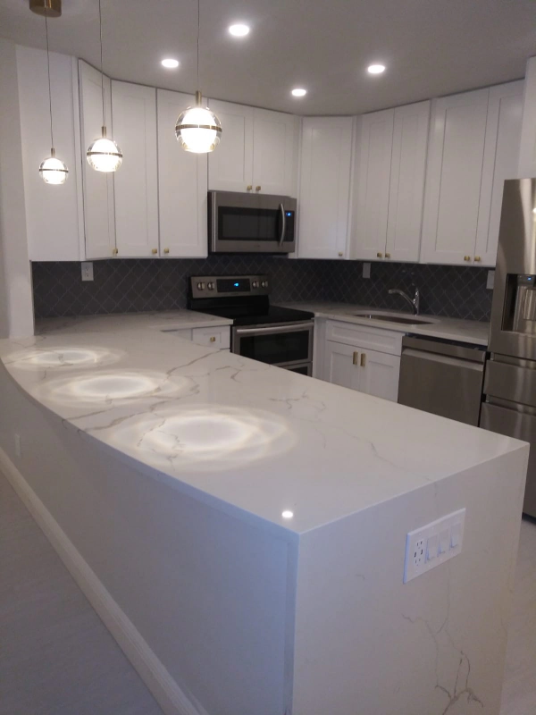 Modern white kitchen with marble countertops, stainless steel appliances, and pendant lights.