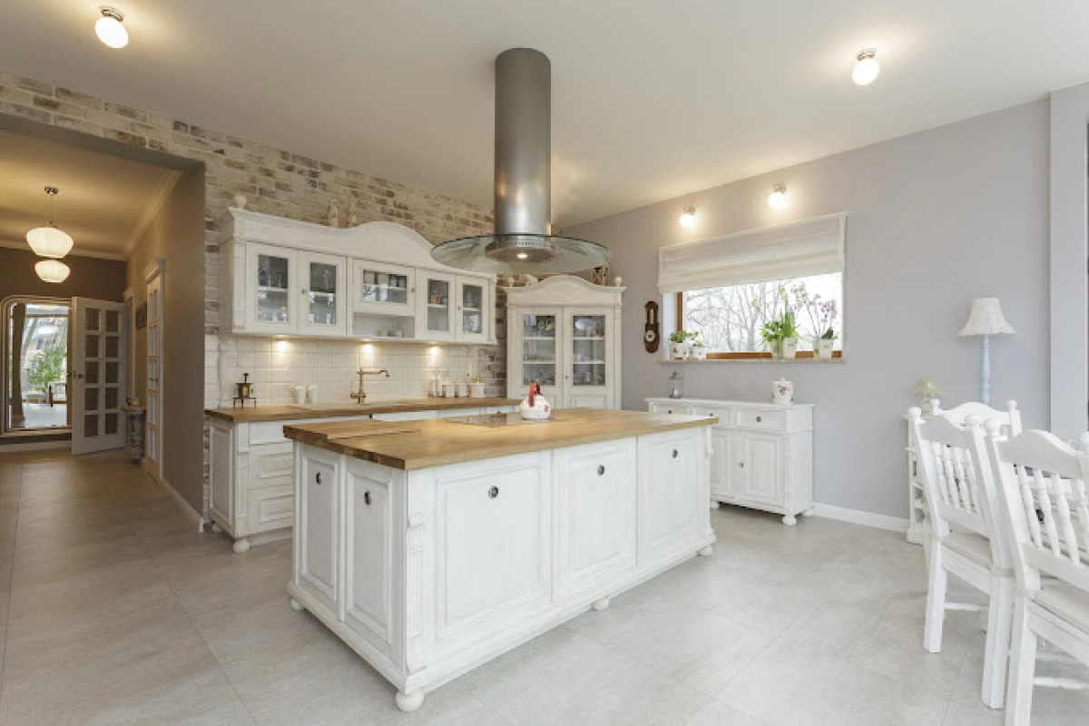 White kitchen with island, wood countertops, and stone wall.