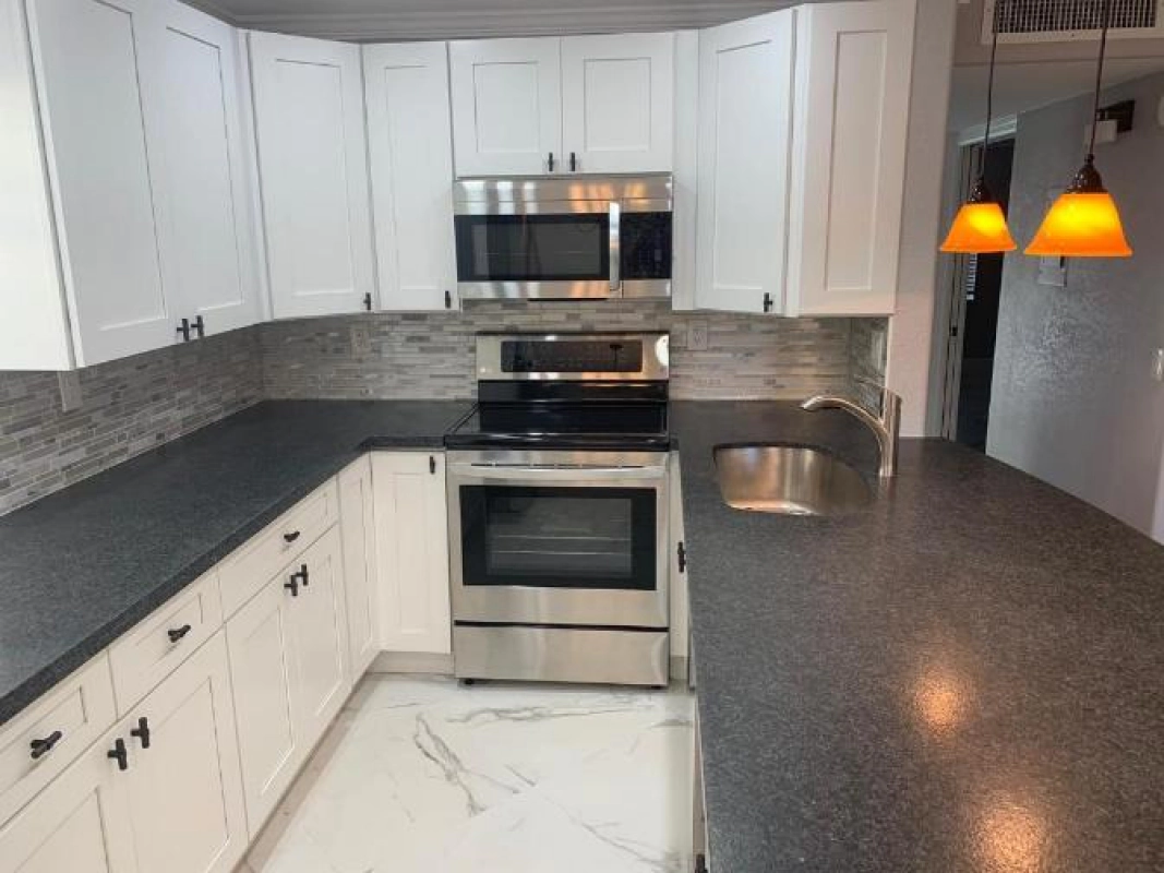 White kitchen with stainless steel appliances, dark countertops, and two pendant lights.