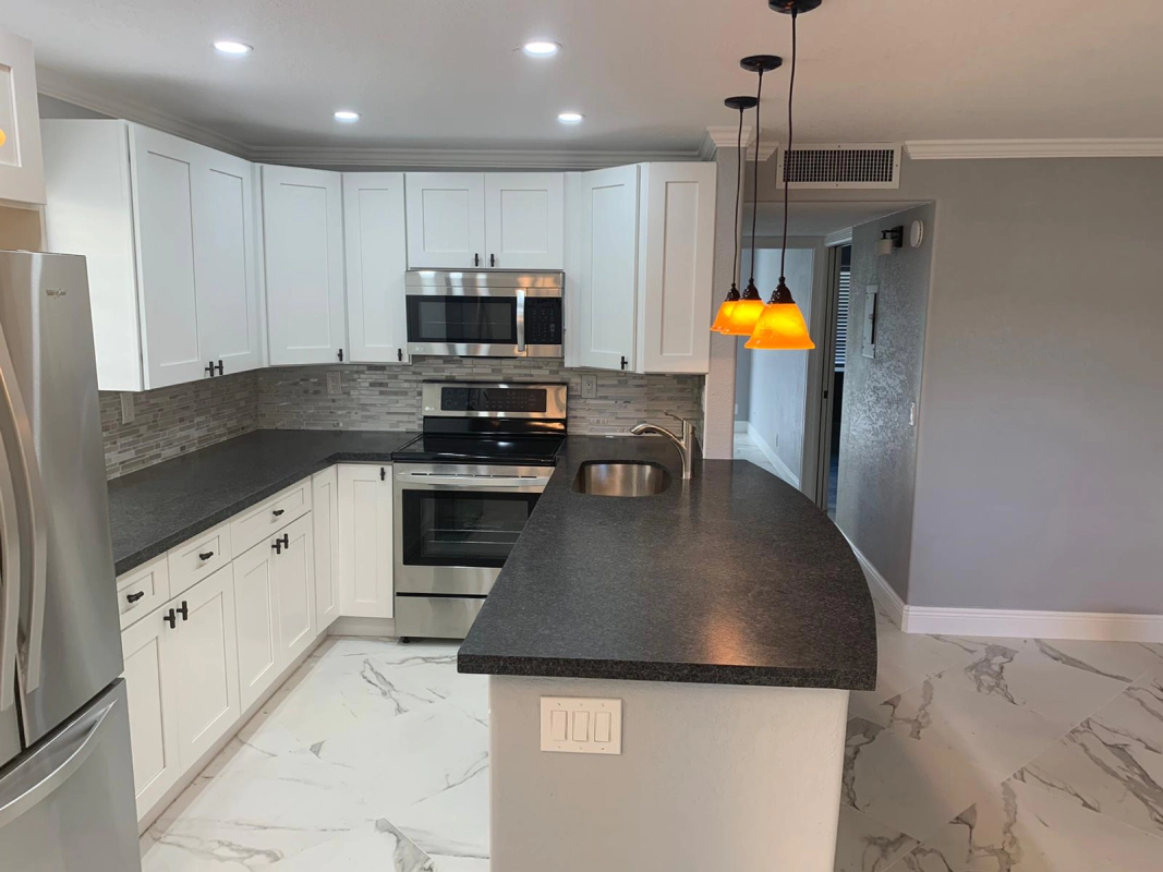 Modern white kitchen with black countertops and stainless steel appliances; pendant lights hang over an island.