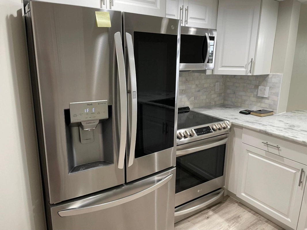 Stainless steel refrigerator and stove in a white kitchen.