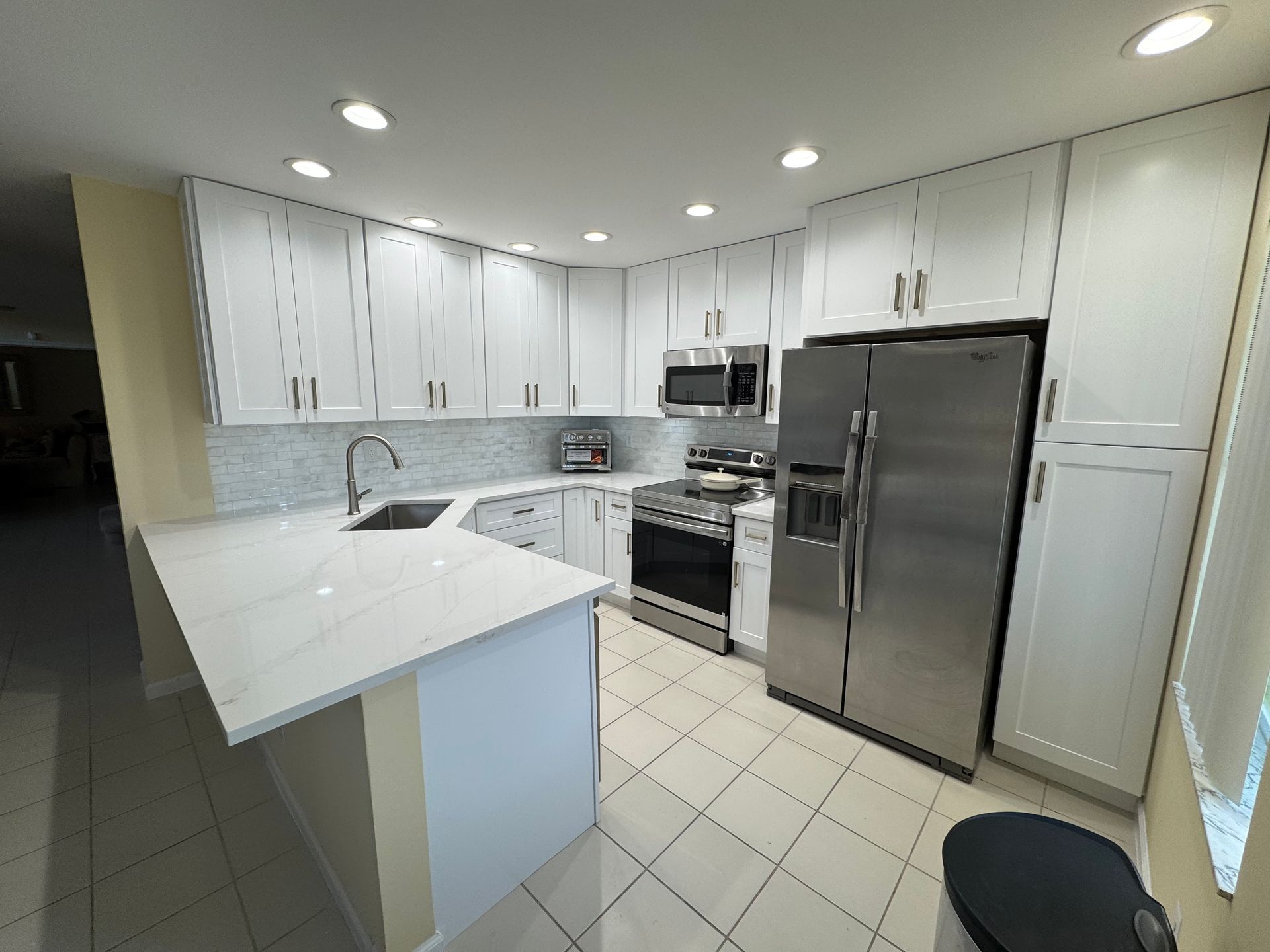 A modern kitchen featuring white cabinets, stainless steel appliances, a peninsula with a white countertop, and tiled floor.