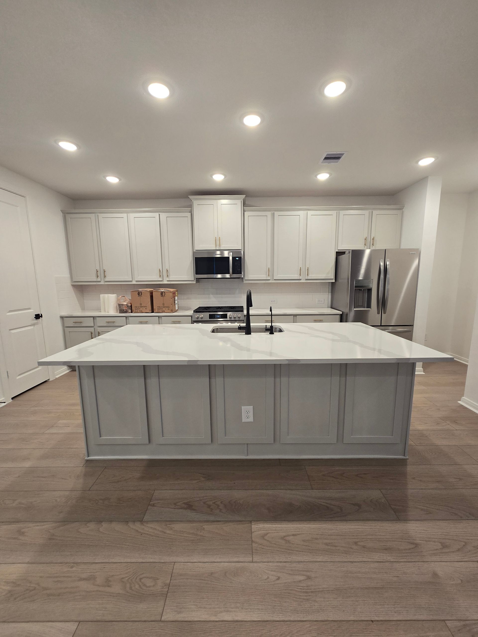 Modern kitchen with dark island, white countertops, and light wood floors in a bright open space