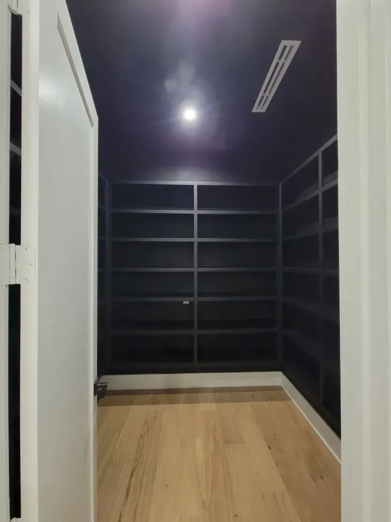 Empty walk-in closet with dark walls, black built-in shelves, and light wood flooring.
