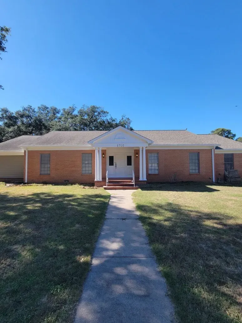 Single-story brick house with a white front porch and a walkway leading through the lawn.