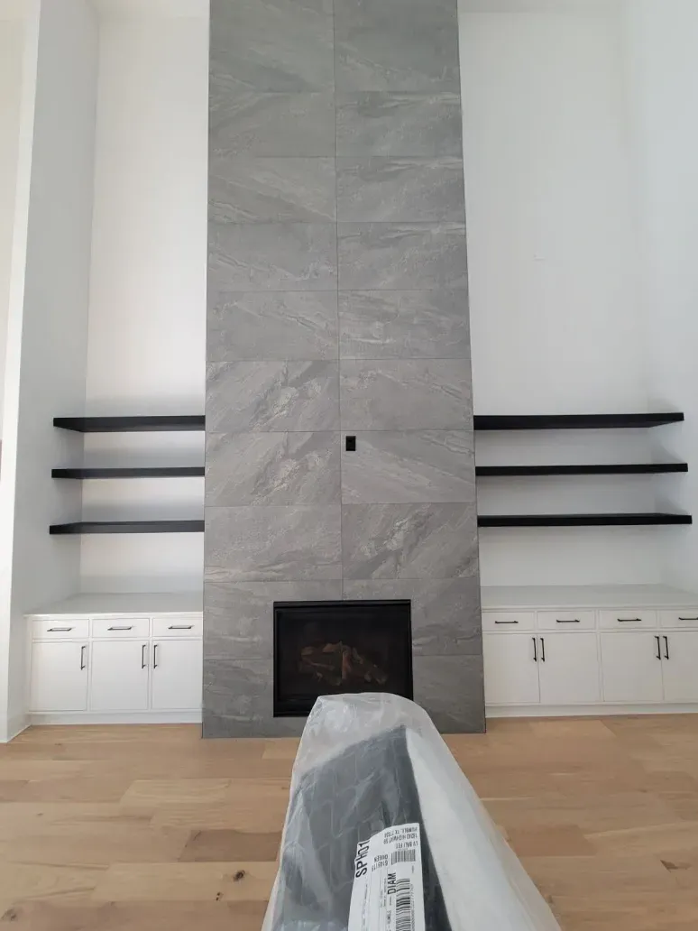 Minimalist living room with tall gray stone fireplace and black wall shelves on white walls.