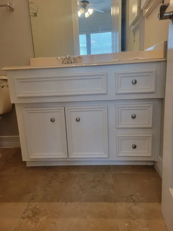 White bathroom vanity with sink and mirror in a tiled room