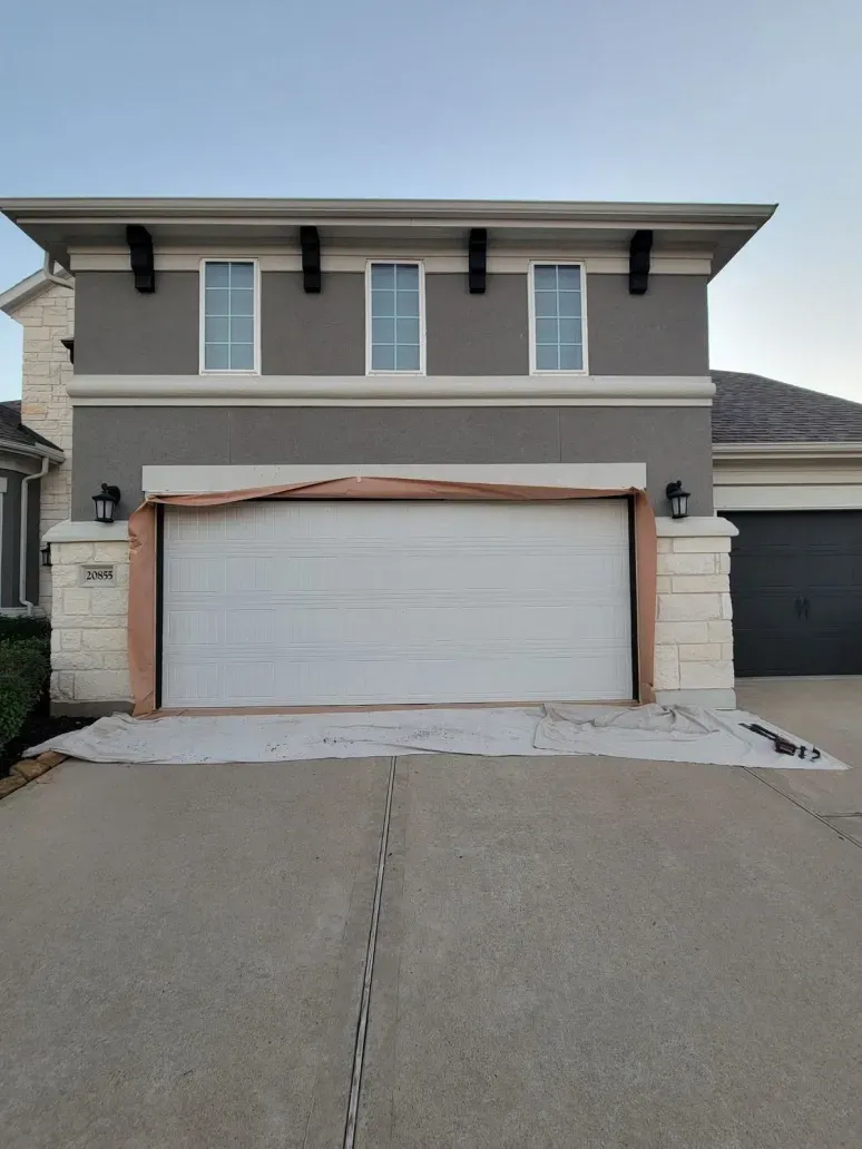 Two-story house with a white double garage door and gray exterior, viewed from the driveway.