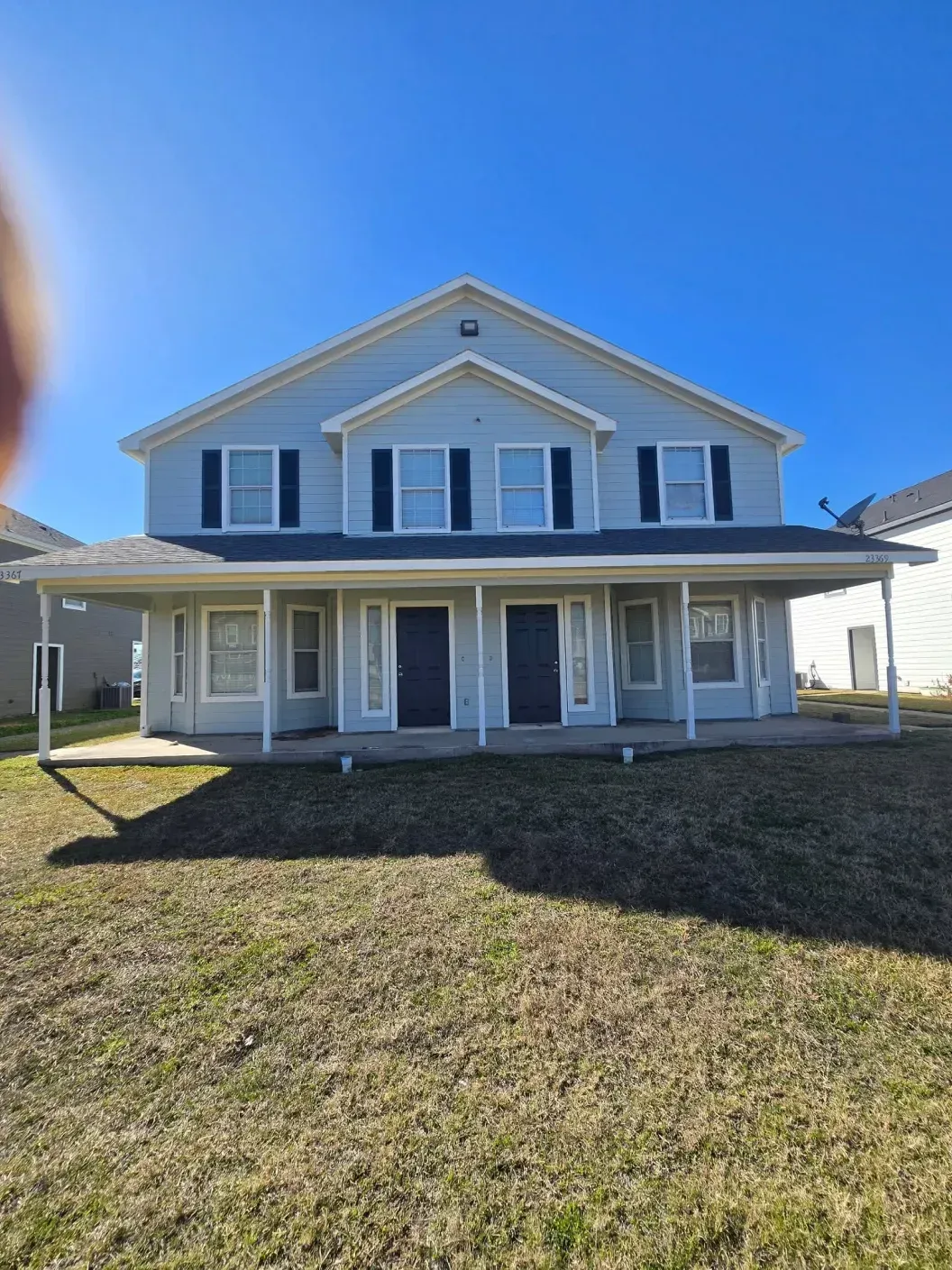Two-story gray house with white trim, front porch, and lawn under a clear blue sky