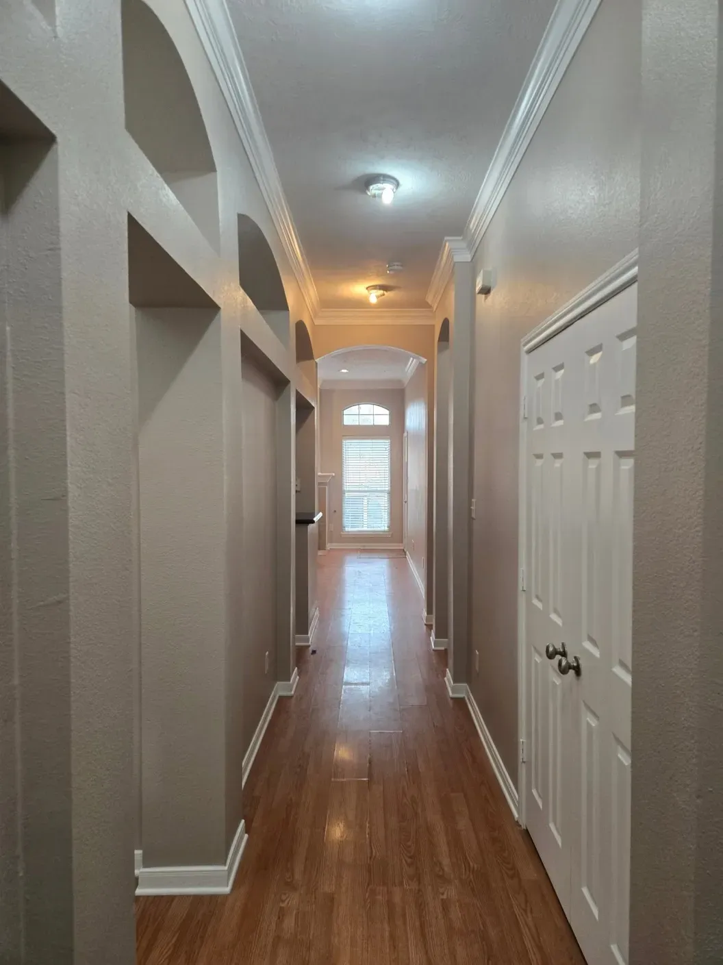 Narrow hallway with wood floors, white doors, and a bright window at the far end