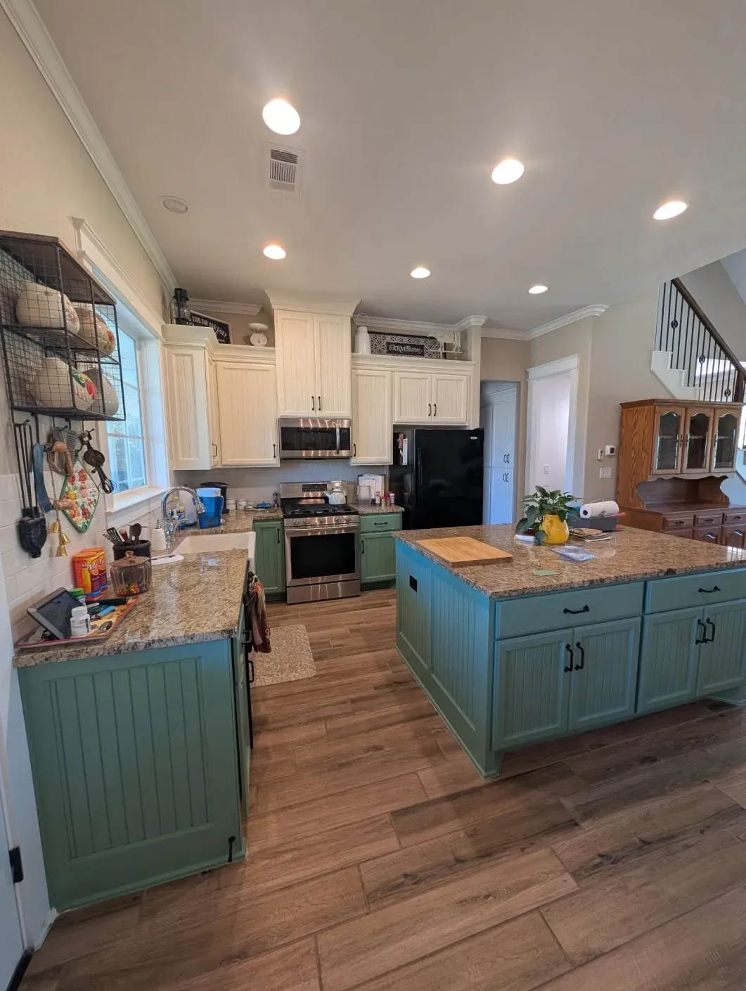Bright kitchen with teal island, white cabinets, wood floors, and recessed ceiling lights.