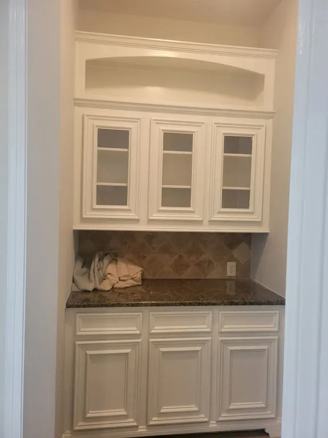 White built-in cabinet with glass doors and dark countertop in a recessed alcove.