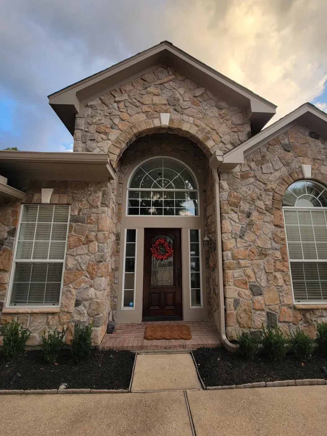 Stone house front entrance with arched doorway, sidelights, and a wreath on the door
