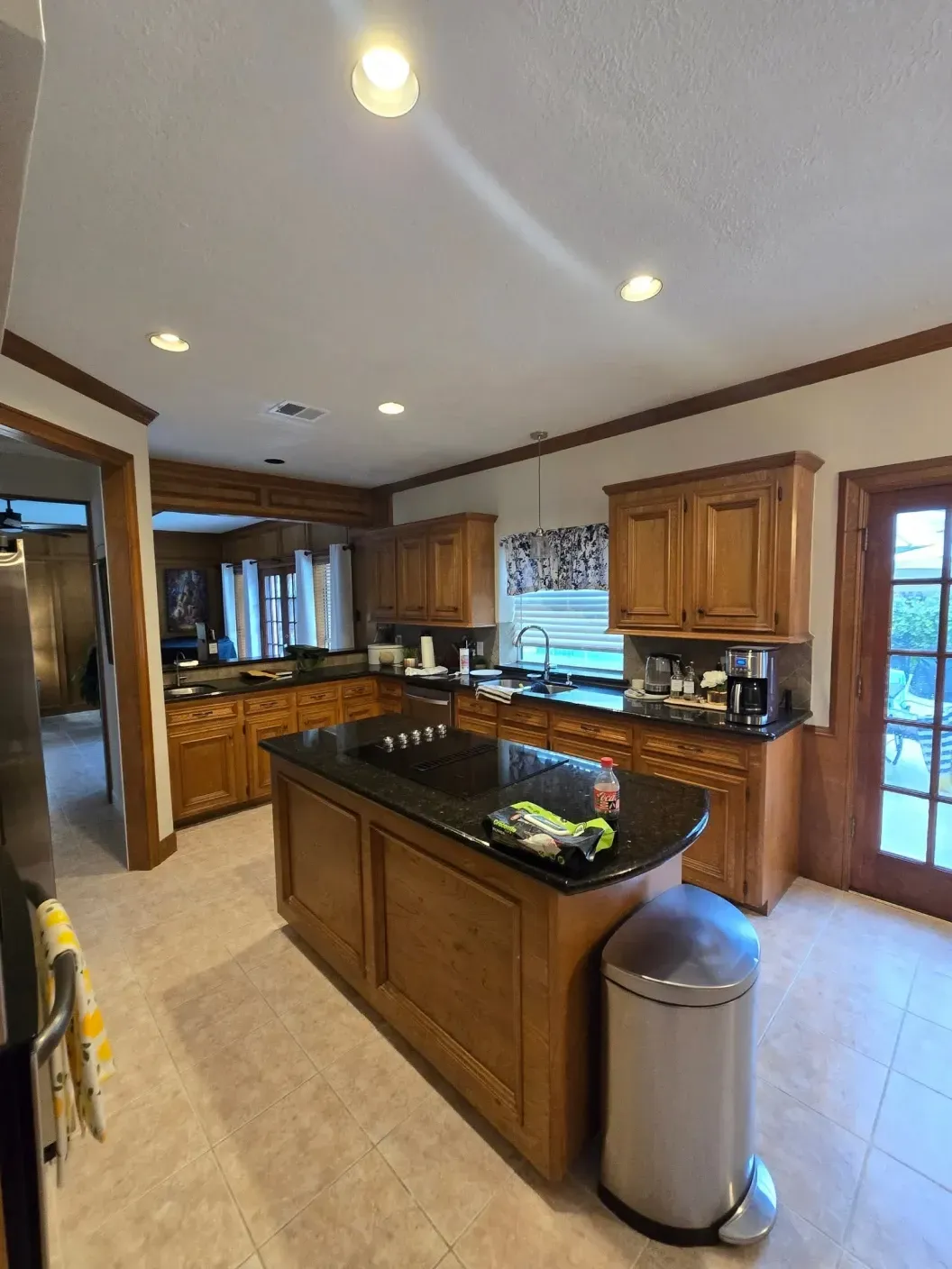 Spacious kitchen with wooden cabinets, black countertops, island, and tiled floor.