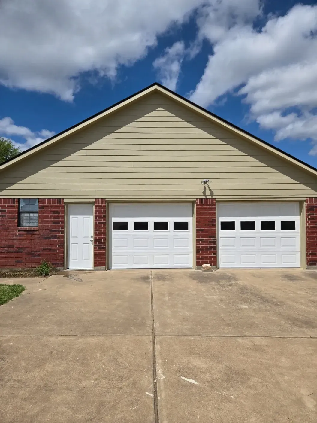 Suburban brick house with two white garage doors and a beige gable, viewed from the driveway
