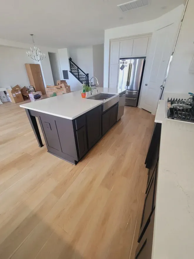 Modern kitchen with a large island, light wood floors, and dark cabinetry in a bright open-plan room