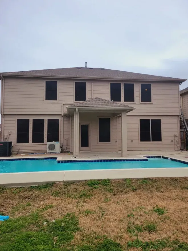 Backyard view of a two-story beige house with a pool and grassy lawn