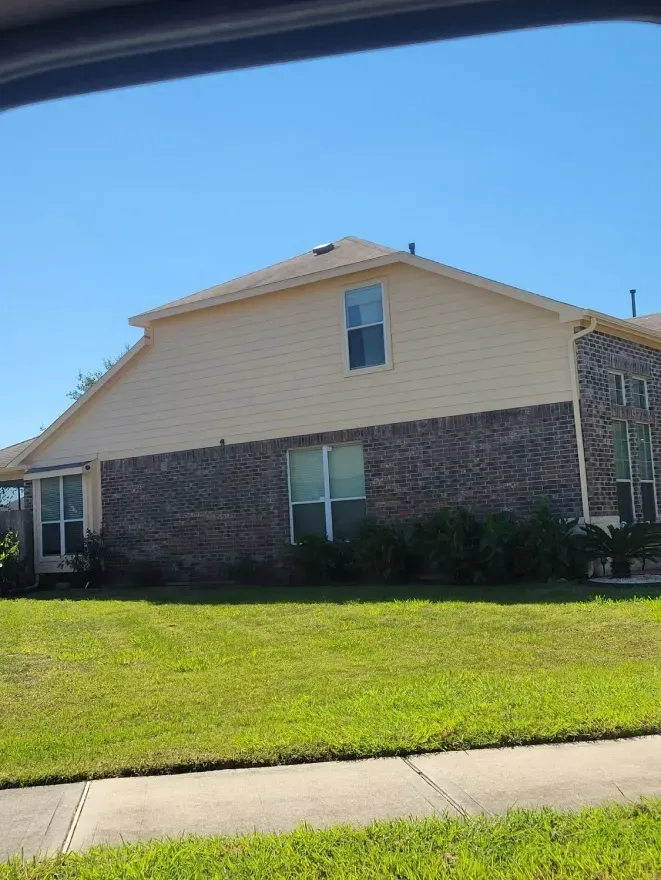 Suburban house with brick and beige siding, green lawn, and sidewalk in front under blue sky