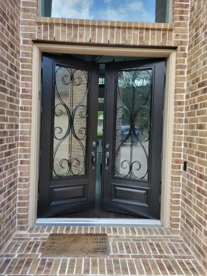 Brick entryway with double dark metal-and-glass doors and decorative ironwork