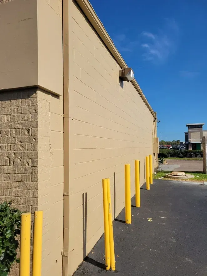 Beige building wall beside asphalt lot with yellow bollards under a blue sky
