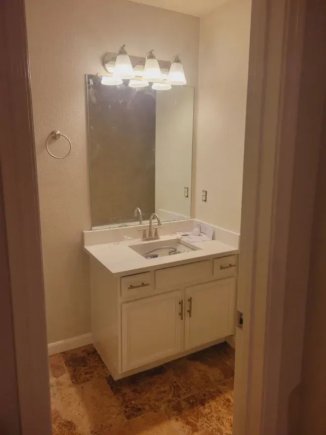 Bathroom vanity with mirror, two lights, white sink cabinet, and beige walls.