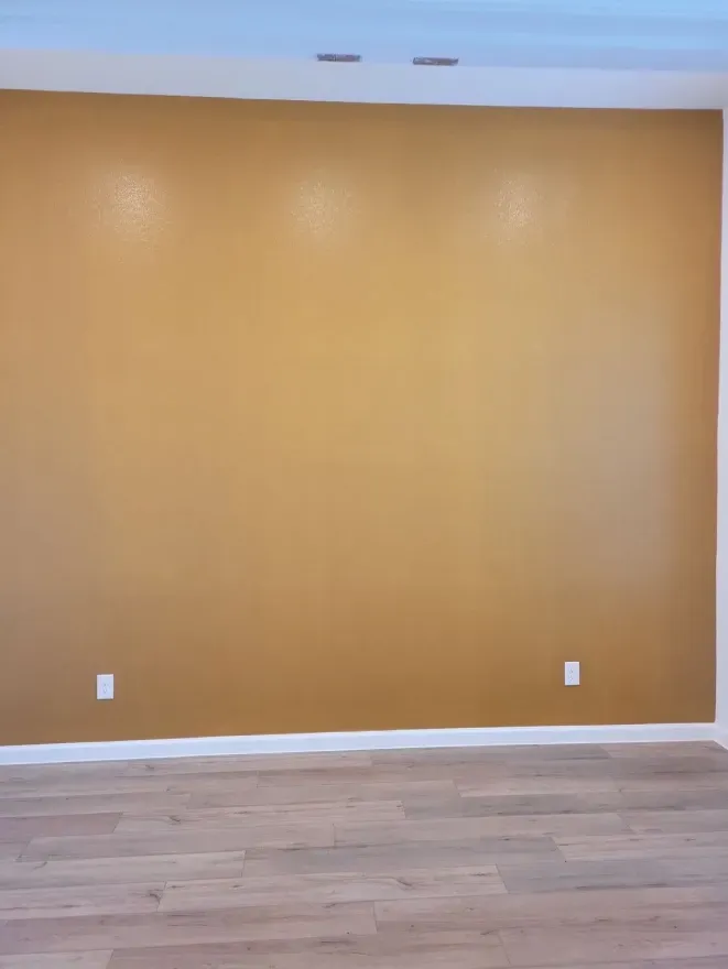 Empty room with tan wall, white baseboards, and light wood flooring