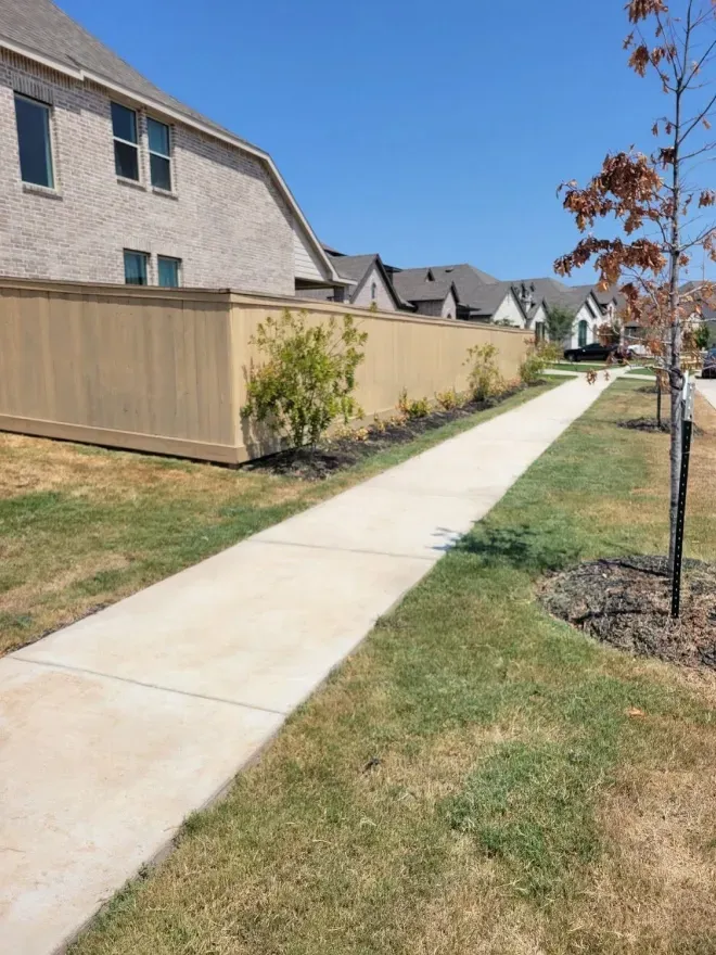 Residential sidewalk beside a tan fence and townhouses on a sunny day
