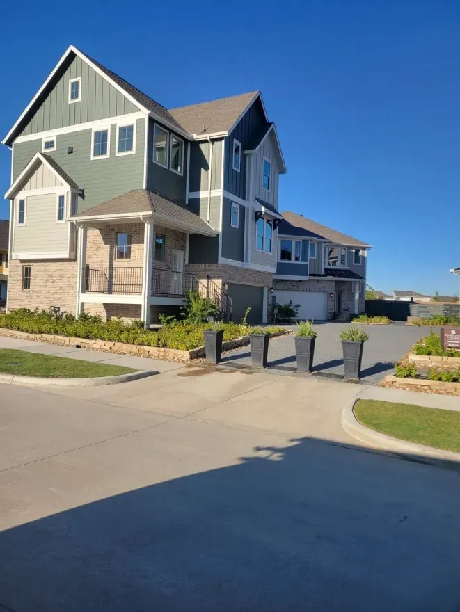 Two-story gray house with stone accents at a suburban street corner under a clear blue sky