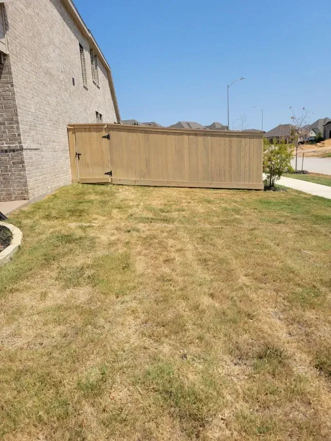Tan mobile beige shed beside a stone building on a dry grassy lawn under a clear sky