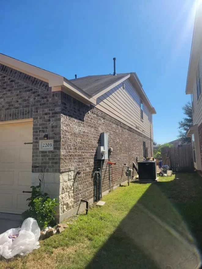 Brick house exterior with side yard, garage door, grass, utility units, and bright blue sky