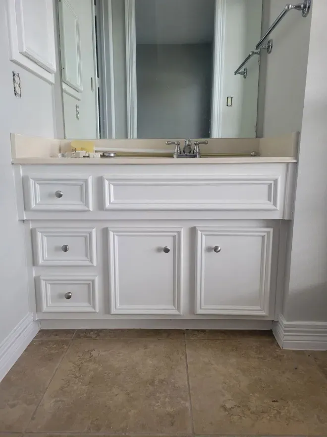 White bathroom vanity with sink and mirror in a tiled room