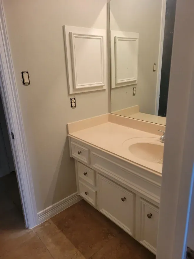 Bathroom vanity with beige countertop, mirror, and white cabinets in a small hallway alcove.