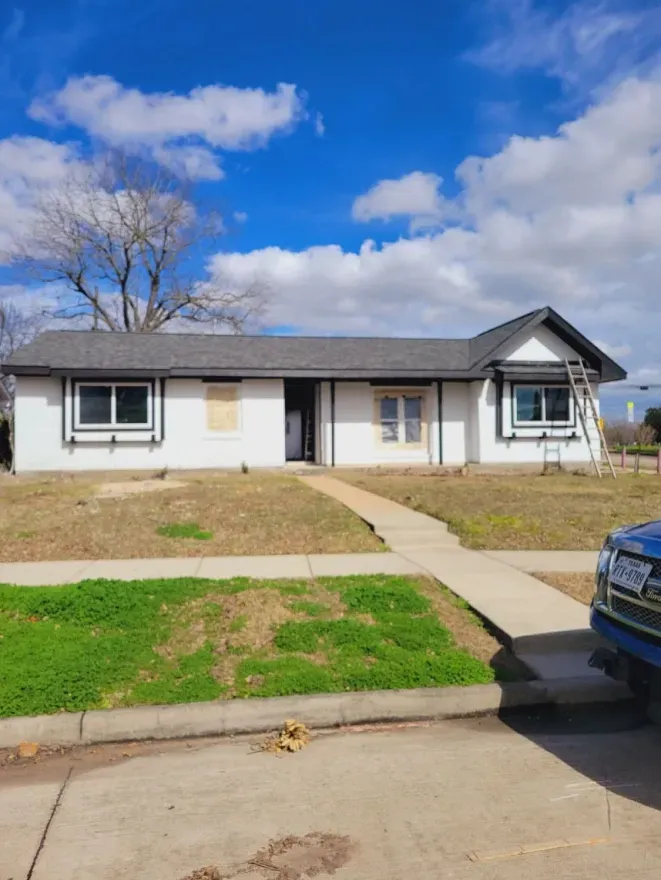 Single-story suburban house with a front lawn, walkway, and blue sky with clouds