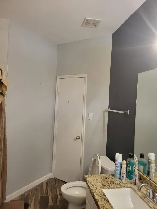 Bathroom with gray walls, white door, toilet, granite counter, and toiletries on the sink.