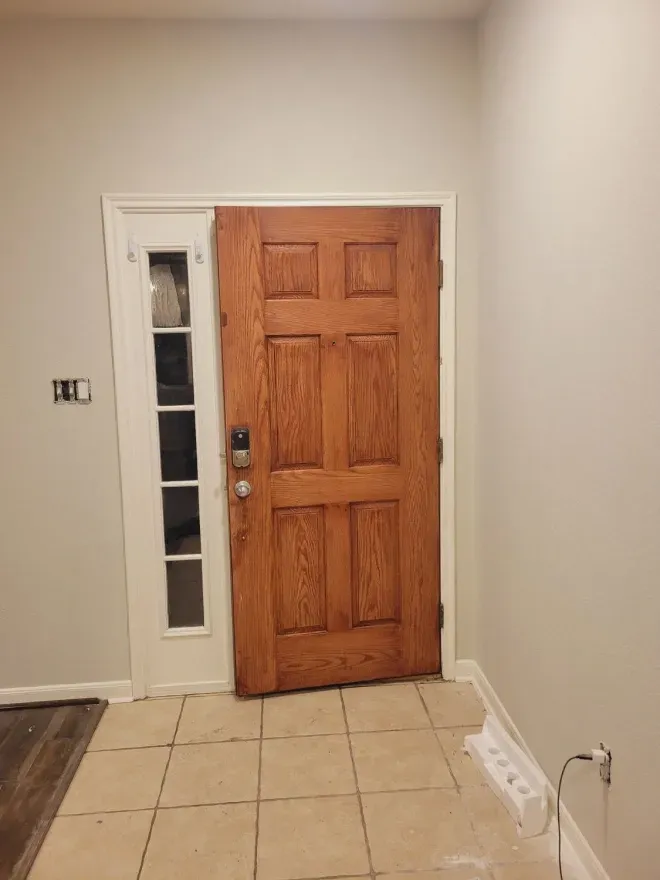 Interior entryway with wooden front door, narrow glass side panel, and tiled floor.