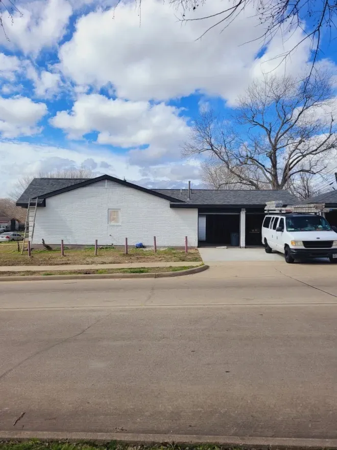 White building with black roof across a street, with a white van parked outside under a cloudy sky
