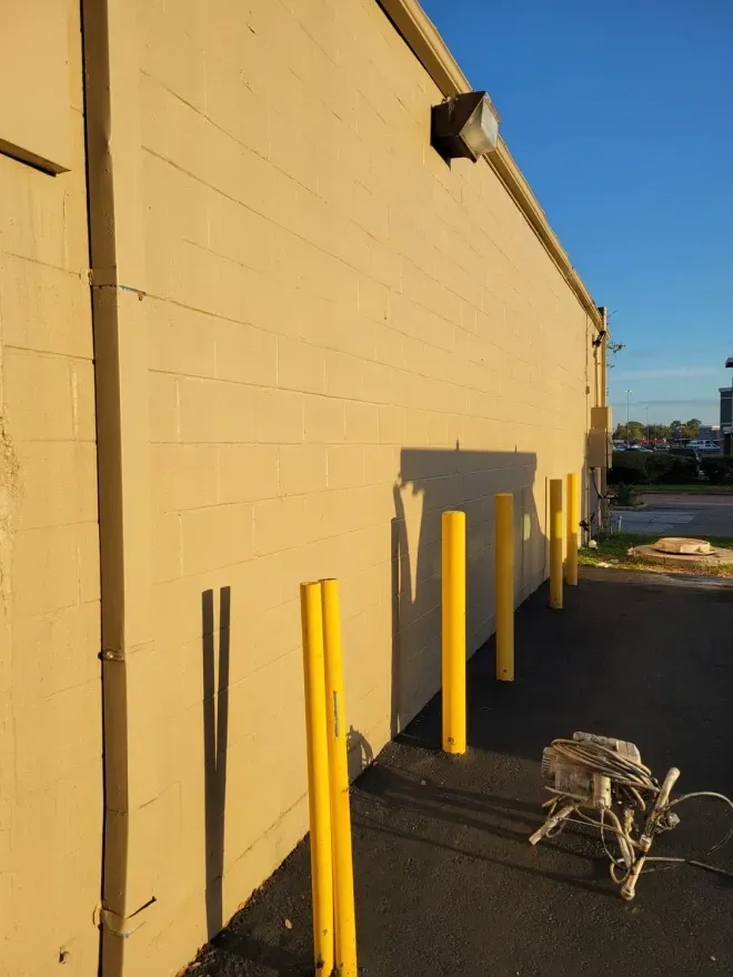 Yellow building wall with yellow bollards and a metal shopping cart in a sunlit alley