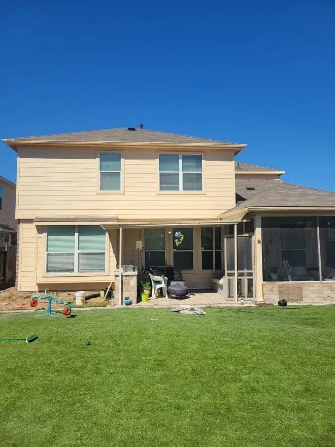 Backyard view of a beige two-story house with a screened porch and green lawn under a clear blue sky