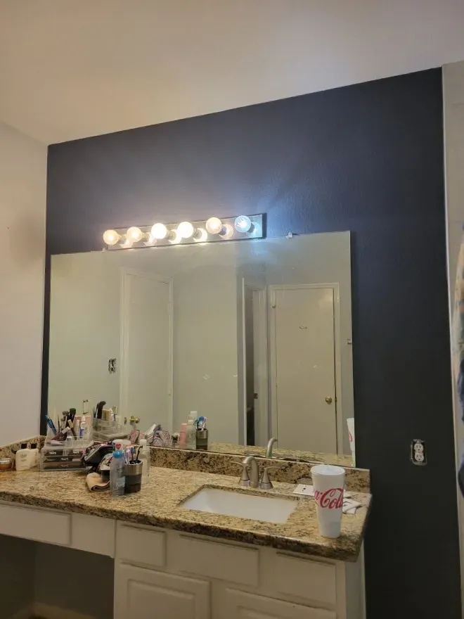 Bathroom vanity with granite countertop, large mirror, and bright light fixture above it.