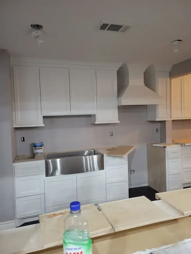 White kitchen under renovation with unfinished cabinets, countertop materials, and a stainless sink area