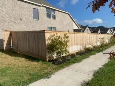 Wooden privacy fence along a suburban sidewalk beside a beige house under a blue sky.