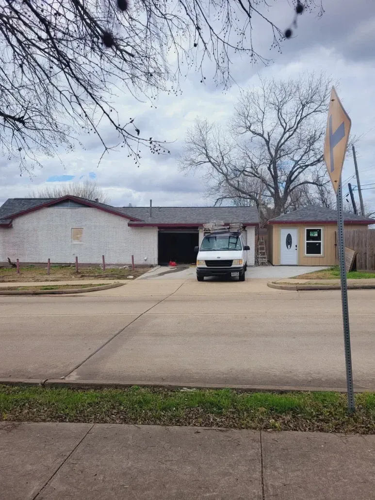 Suburban single-story house with a white car parked in the driveway under a cloudy sky.