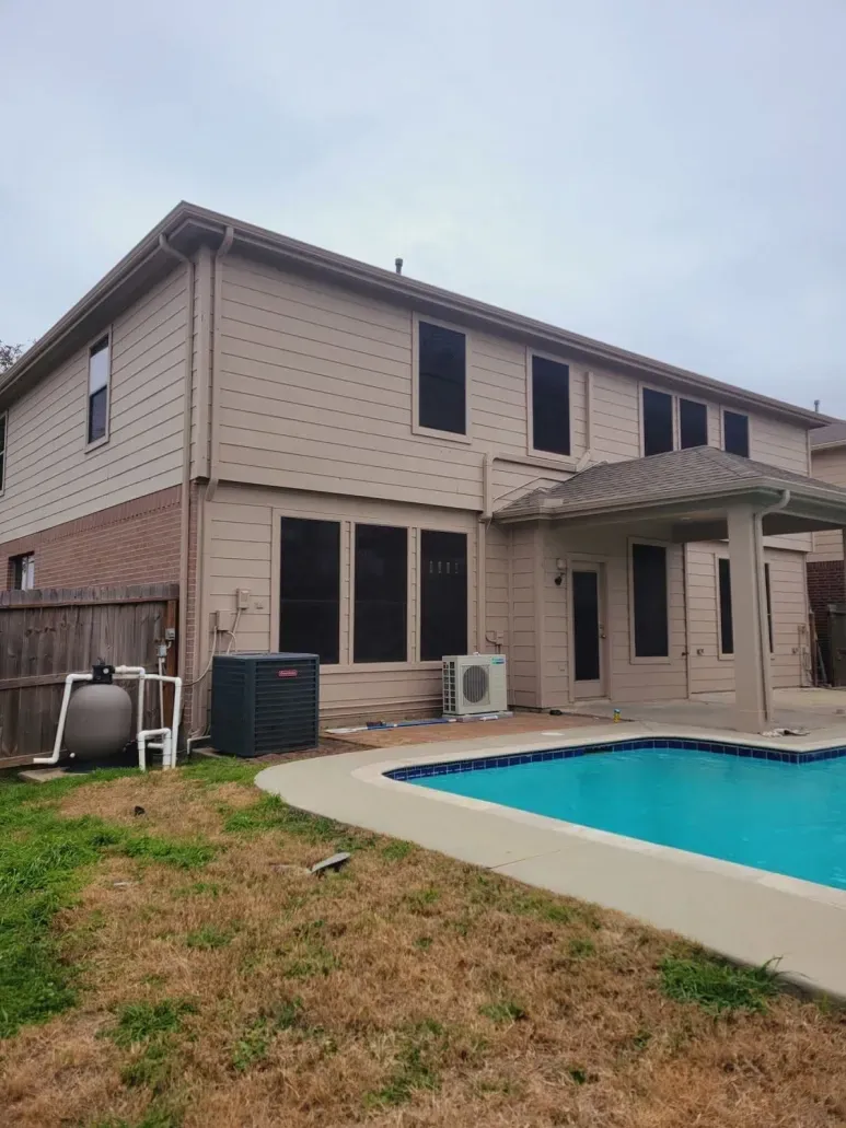 Two-story beige house with a backyard pool, patio, and lawn under an overcast sky
