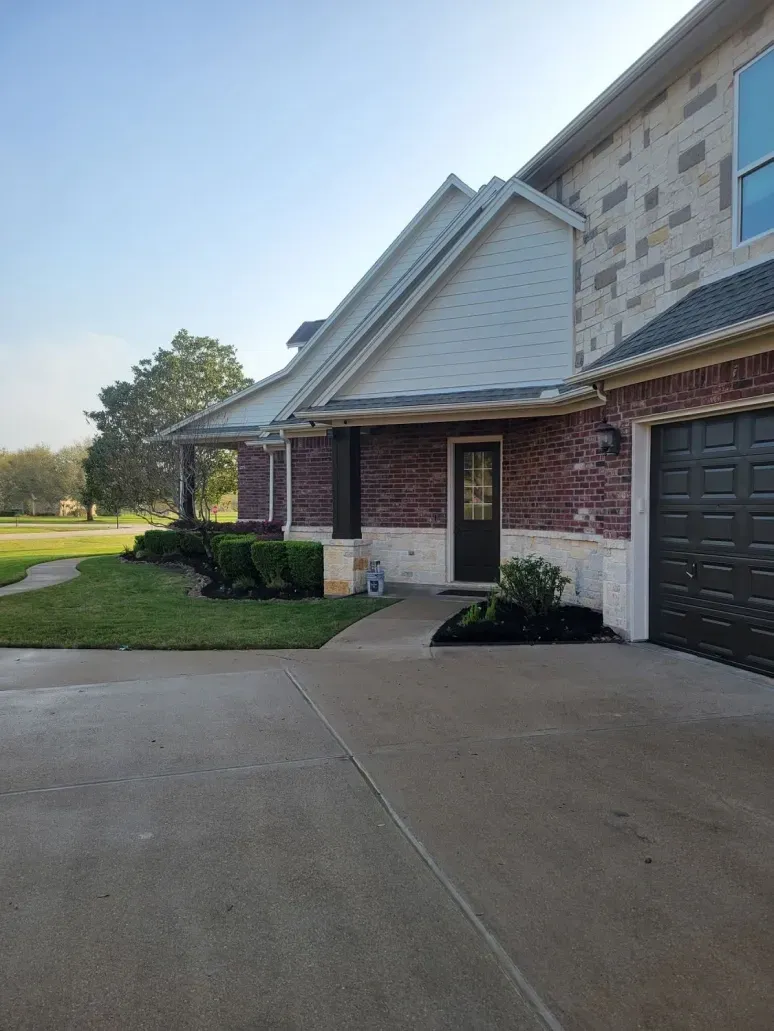 Brick and stone house exterior with a driveway, front porch, and garage in daylight