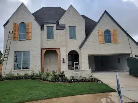 Two-story beige house with black roof, arched entry, large windows, garage, and a green lawn
